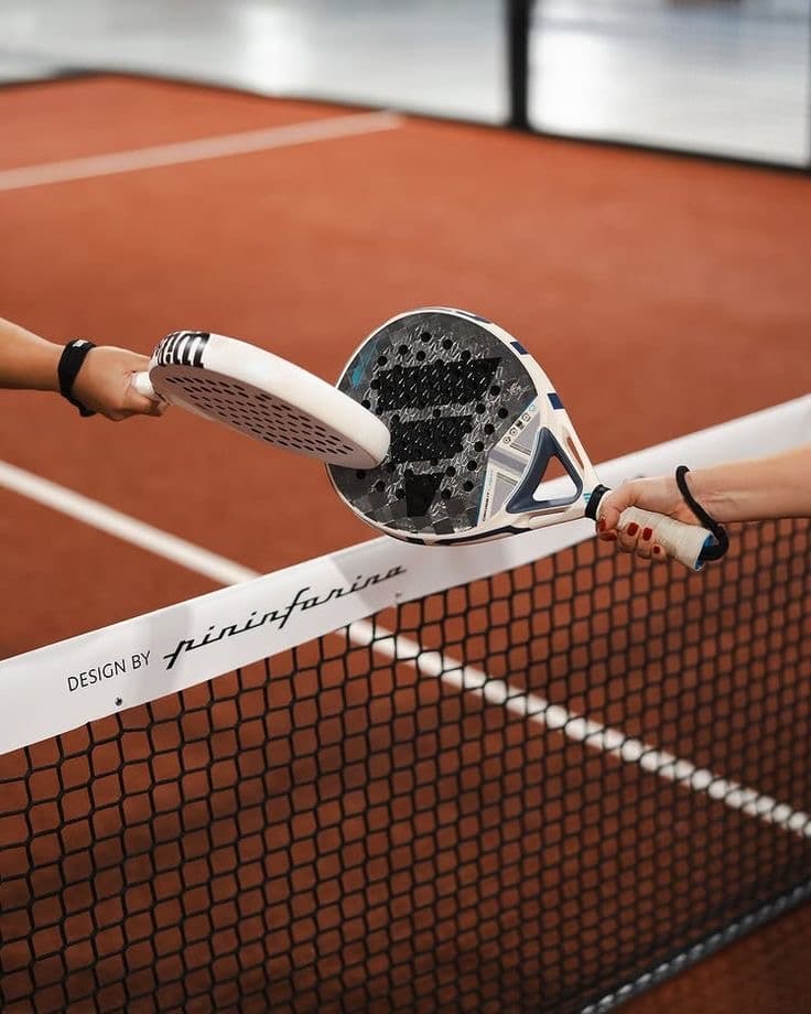 Two players' rackets meeting over the net on a padel court